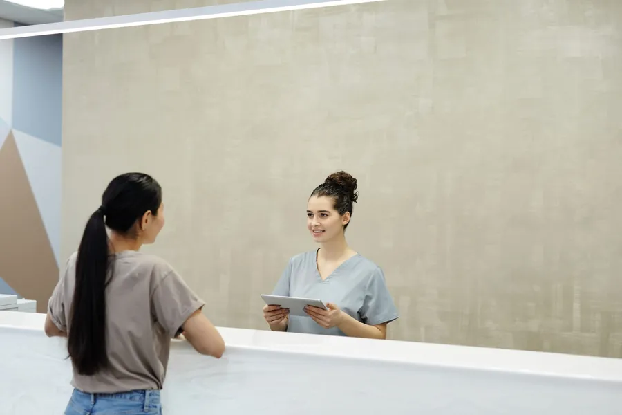 A staff member with a tablet welcomes a visitor at a reception desk